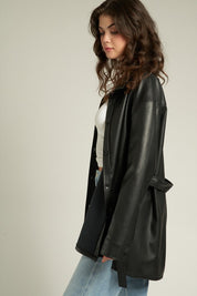 Woman in a Lyra Faux Leather Jacket styled with a cinched waist, showcasing a trendy and relaxed silhouette.