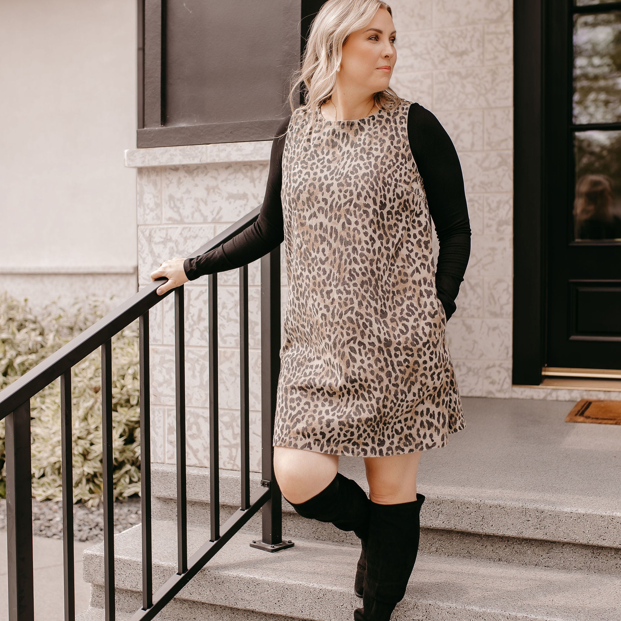 Woman in leopard print dress and black boots posing on stairs, featuring clearance bottoms from the sale collection.