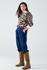 Model wearing the Scarlett Leopard Sweater with relaxed fit pants and cowboy boots, showcasing chic leopard print and red accents.